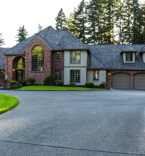 Wide gray concrete driveway in front of a large brick home