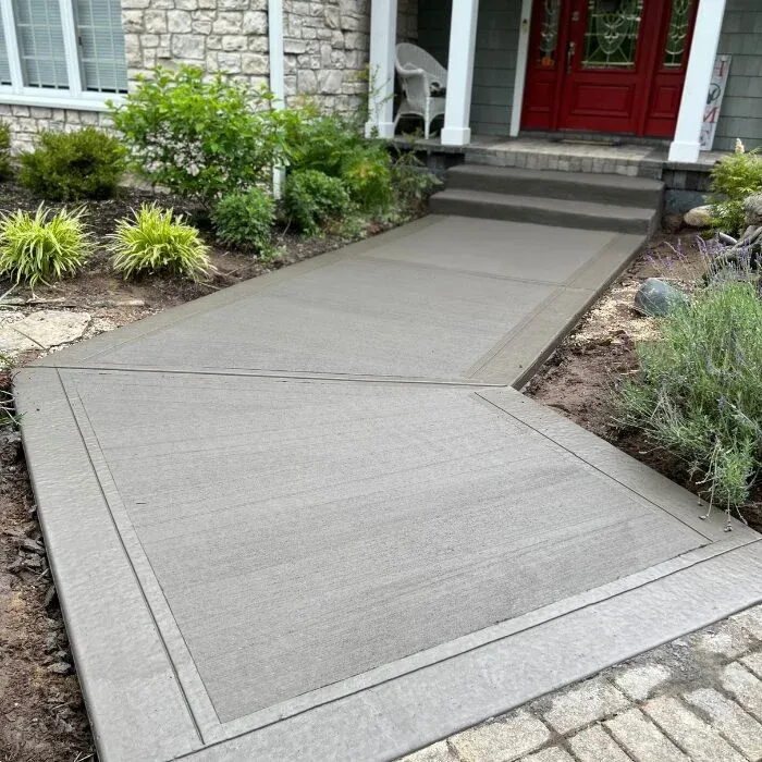 Gray concrete walkway leading to broom-finished porch steps and a red front door