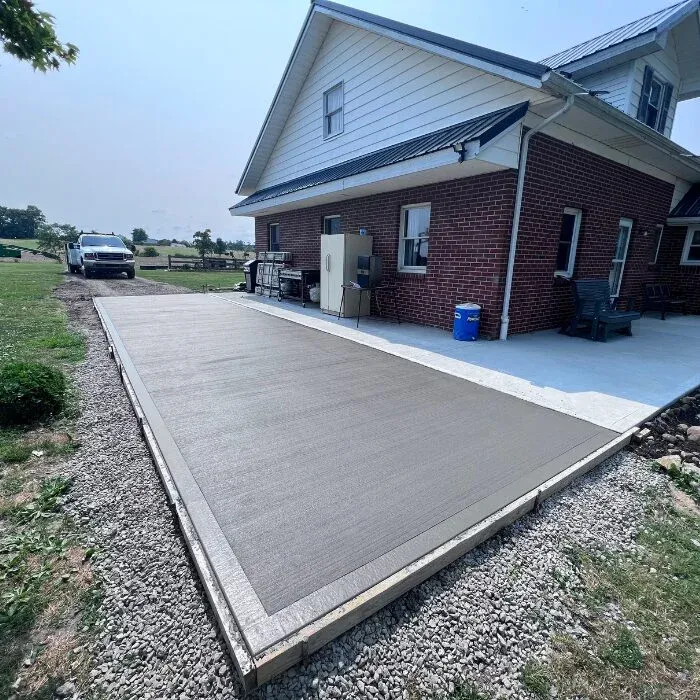 Broom-finished concrete patio with a border beside a brick farmhouse