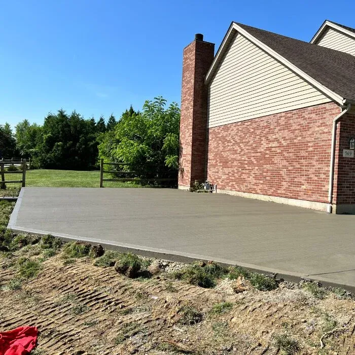 Broom-finished concrete patio beside a brick home under a blue sky