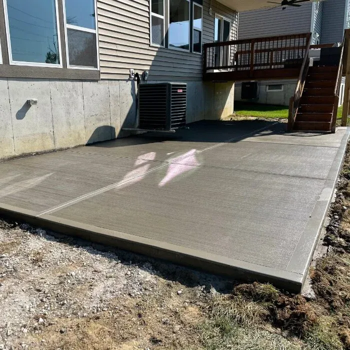 Broom-finished concrete patio behind a home below a raised deck