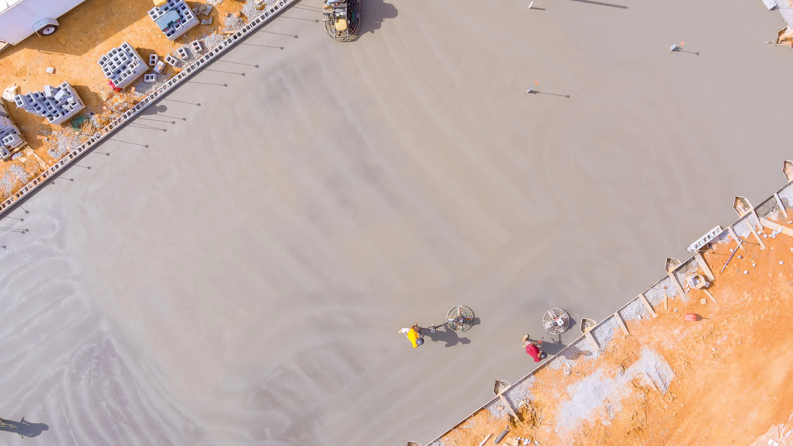 Aerial view of a crew power-troweling a large freshly poured concrete slab on a construction site