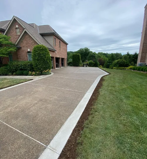 Wide exposed-aggregate concrete driveway with smooth borders beside a large brick home